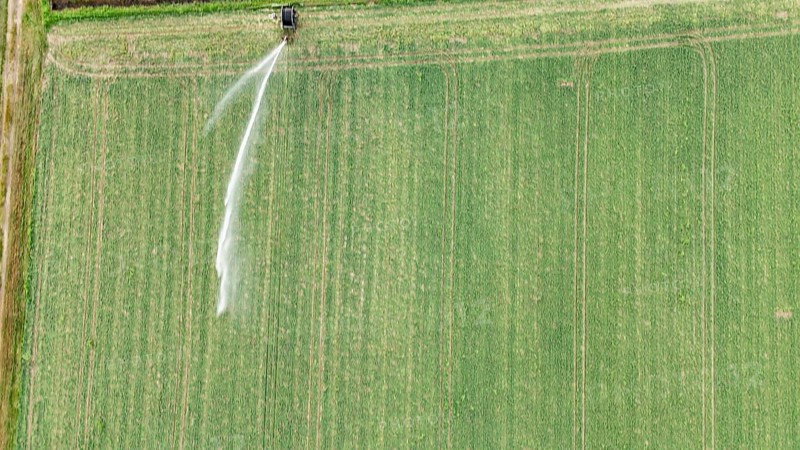 Aerial view of a large agricultural field with a rain gun sprinkler system irrigating young soybean plants in the Po Valley Italy during a warm springtime season