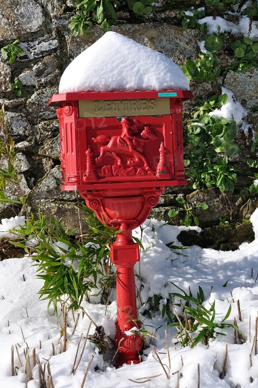 Vintage red mailbox under the snow, Ornate red mailbox covered in snow against a stone wall with green plants