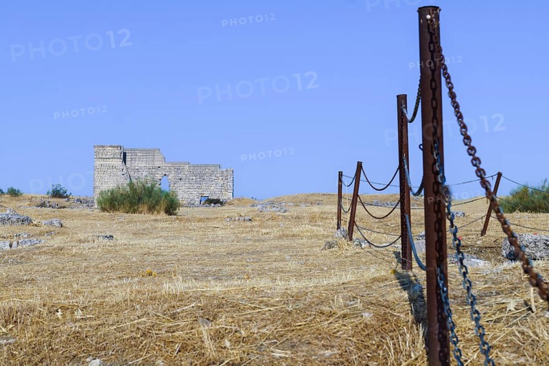 Rusty fence protecting an archeological site with ancient ruins under a clear blue sky, Malaga, Spain