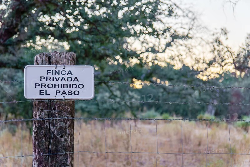 No trespassing sign in spanish (finca privada, prohibido el paso) attached to a barbed wire fence post
