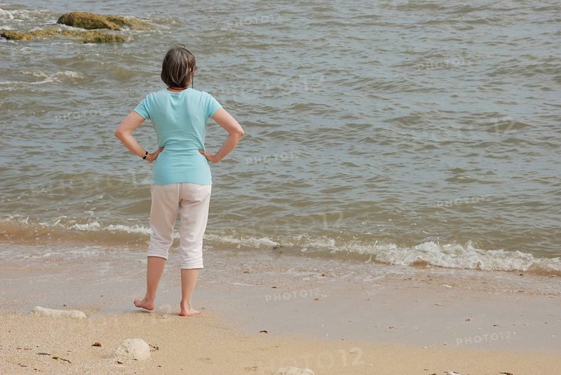 A woman stands on a sandy beach looking at the ocean waves, with rocks in the background in Royan in Charentes, France