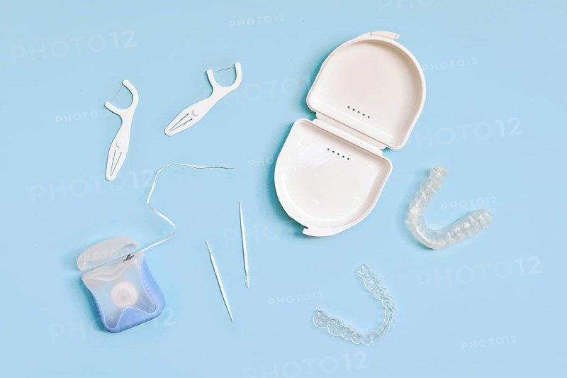 Top view of dental clear aligners, case, toothpicks and floss on blue background