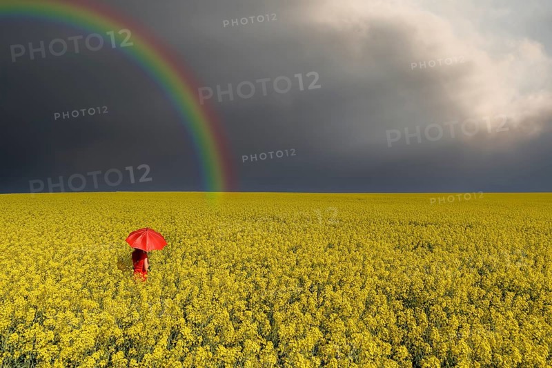 Woman with red umbrella in rape field rainbow