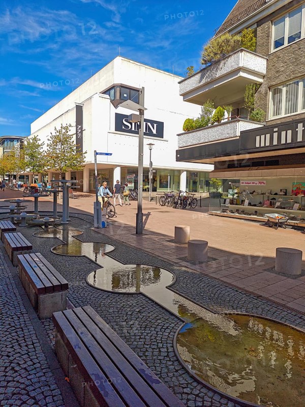 Pedestrian zone with fountain, department stores', pedestrians, traffic-calmed, young trees, residential building, balconies, old town, architecture, shops, people, blue sky, sunshine, Brühl, North Rhine-Westphalia, Germany