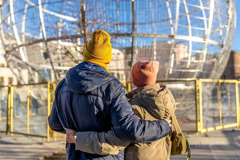 Elderly couple embracing while admiring large christmas ball decorations in a winter cityscape