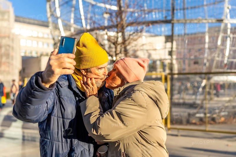 Happy senior couple kissing and taking a selfie with smartphone in a winter city during christmas holidays