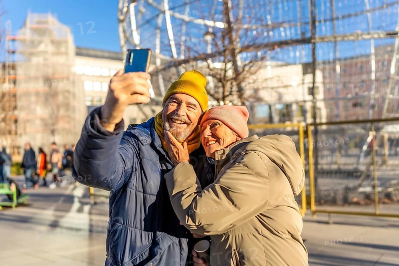 Smiling senior couple taking a selfie with smartphone in a winter city center during christmas holidays