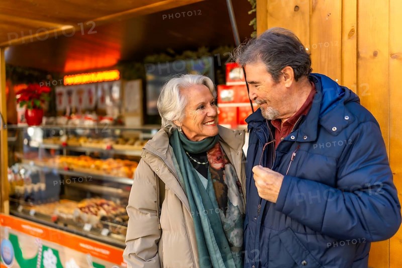 Elderly couple smiling and looking at each other in front of a food stall at a christmas market