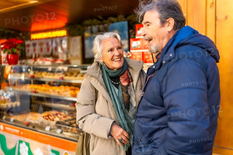 Smiling senior couple chatting in front of a bakery stall at a christmas market in winter