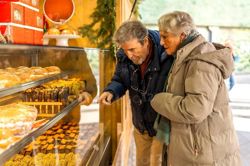 Elderly couple pointing and choosing delicious pastries from a market stall display during the christmas holidays