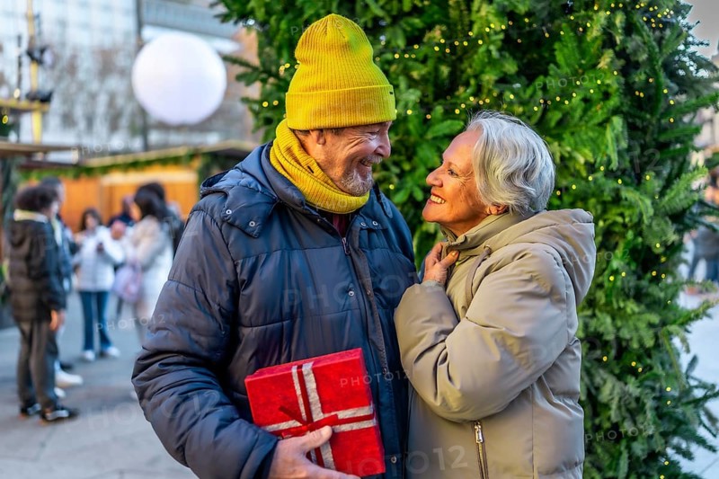 Elderly man surprising his wife with a christmas present at a christmas market during winter holidays