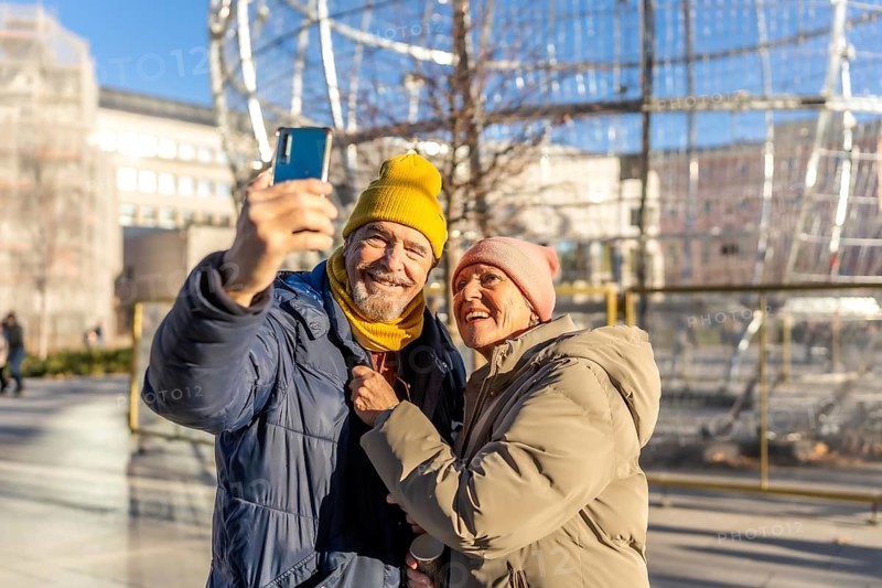 Smiling senior couple taking selfie with smartphone in winter city center during christmas holidays