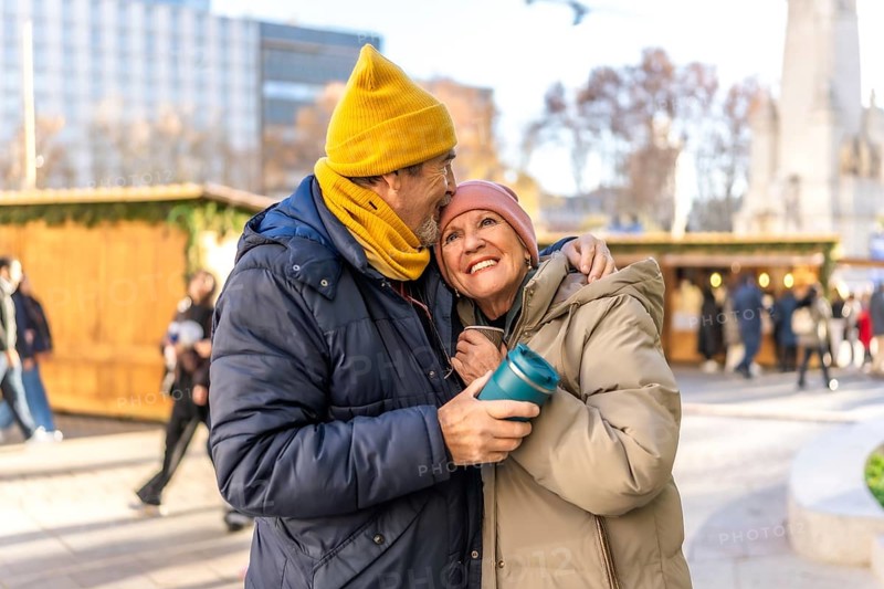Affectionate senior couple enjoys warm drinks at a christmas market in a winter city setting
