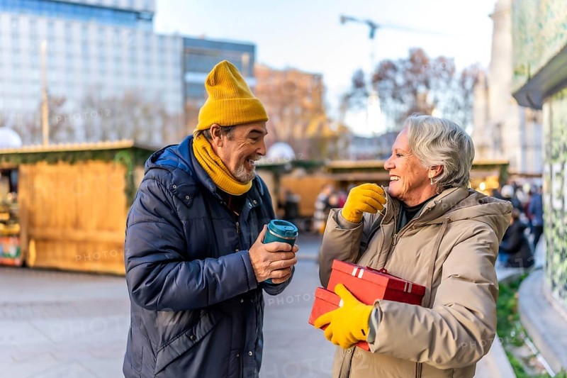 Elderly couple exchanging christmas presents and enjoying a hot beverage at a traditional christmas market during winter holidays
