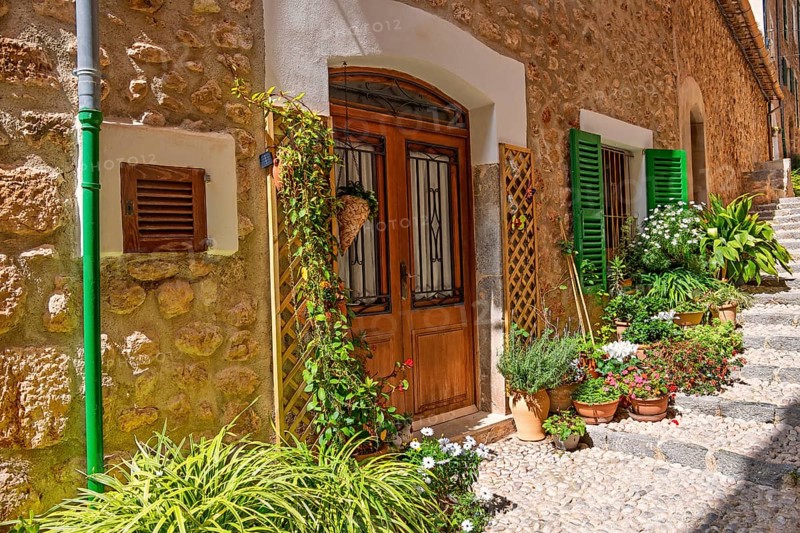 Apartment door with flowers and green plants outside on a stair in a cobblestone alley a sunny summer day, Fornlalutx, Mallorca, Spain