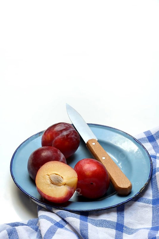 Red plums on plate with kitchen knife, Prunus domestica