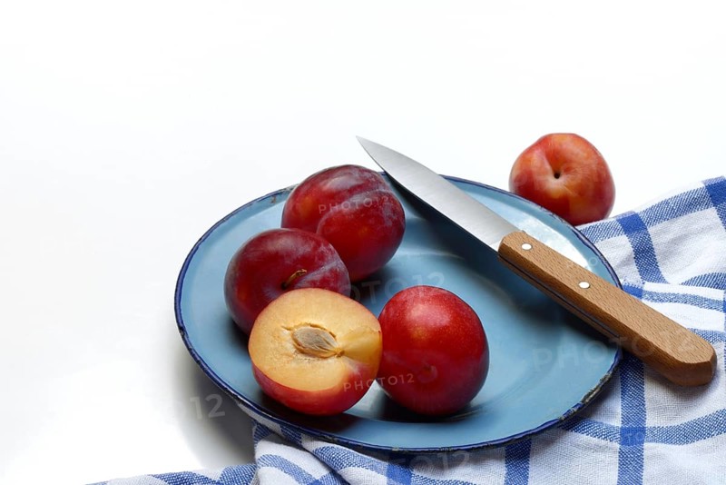 Red plums on plate with kitchen knife, Prunus domestica
