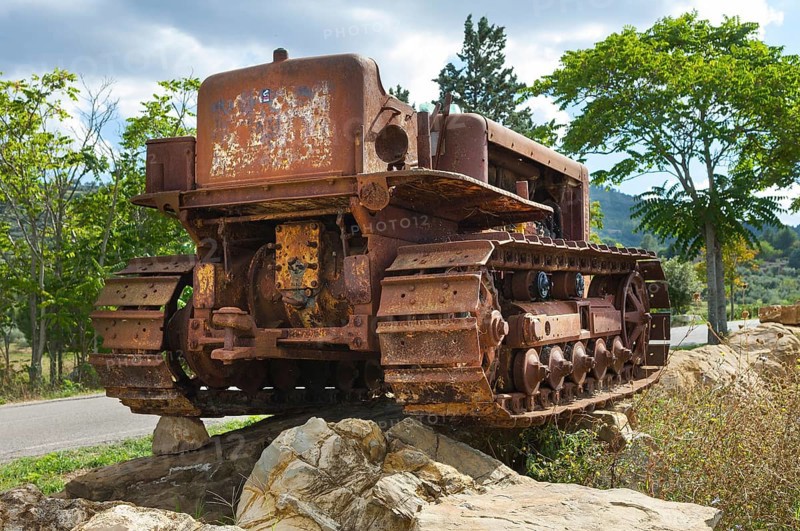Old, heavily rusted bulldozer for road construction stands abandoned on rocks, industrial relic