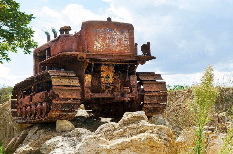 Old, heavily rusted bulldozer for road construction stands abandoned on rocks, industrial relic