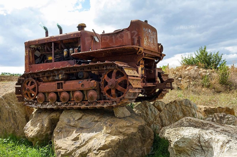 Old, heavily rusted bulldozer for road construction stands abandoned on rocks, industrial relic