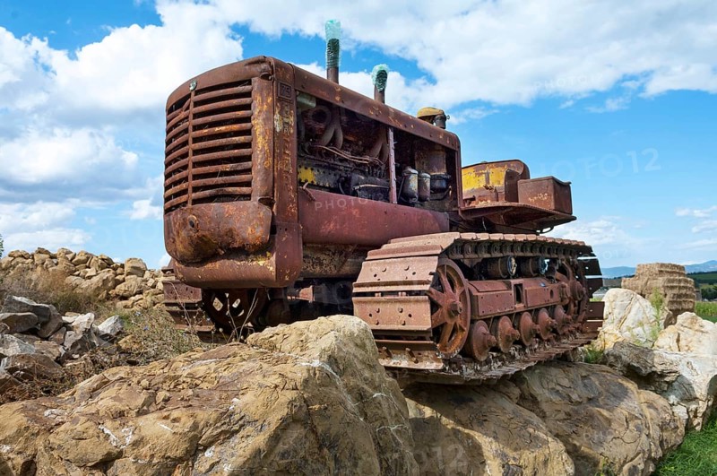 Old, heavily rusted bulldozer for road construction stands abandoned on rocks, industrial relic