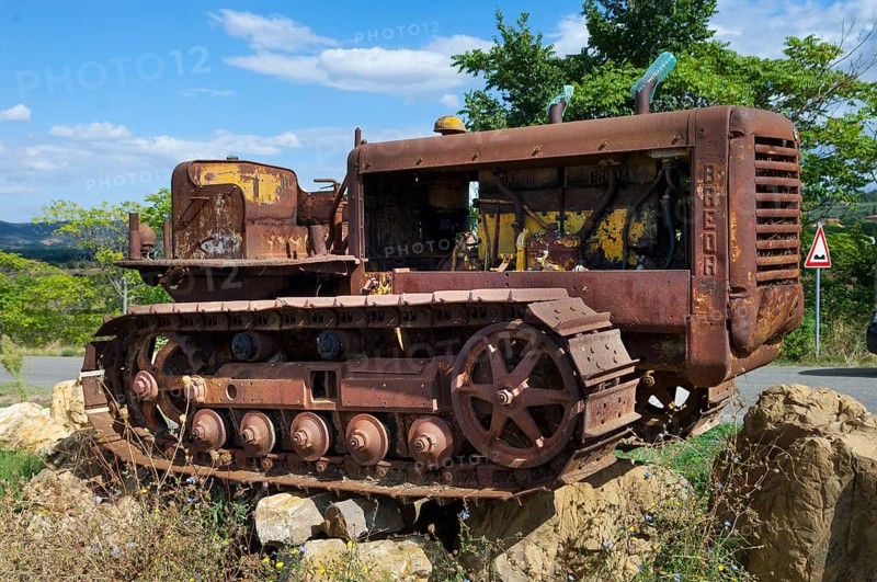 Old, heavily rusted bulldozer for road construction stands abandoned on rocks, industrial relic