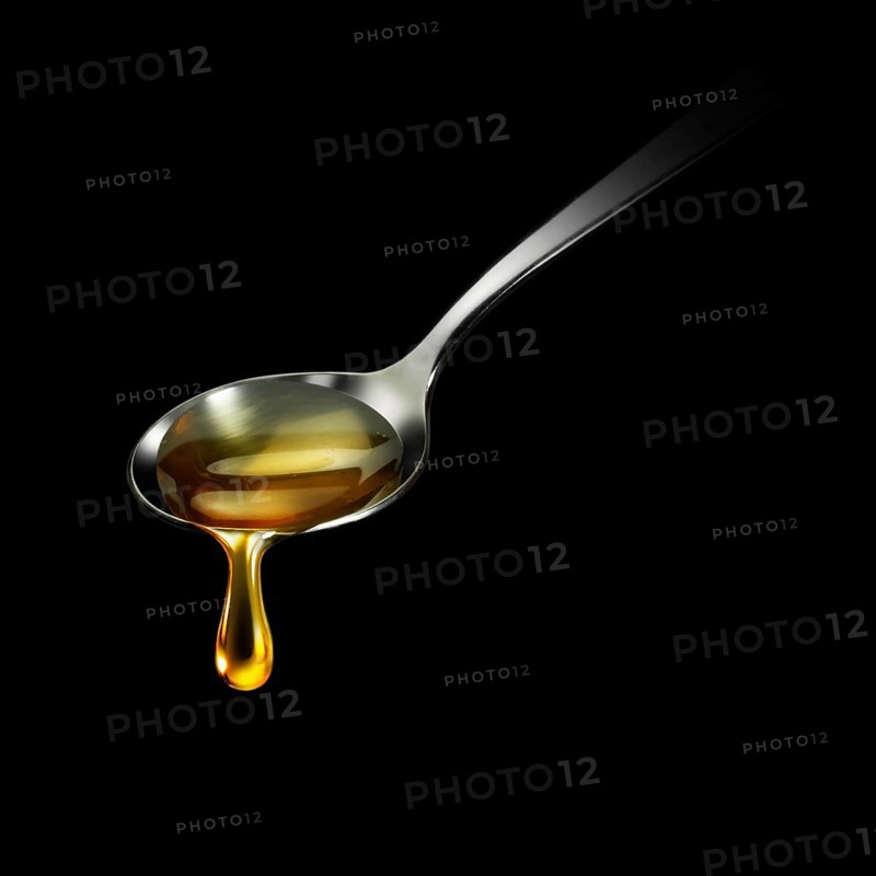 Honey drips from a spoon in front of a black background