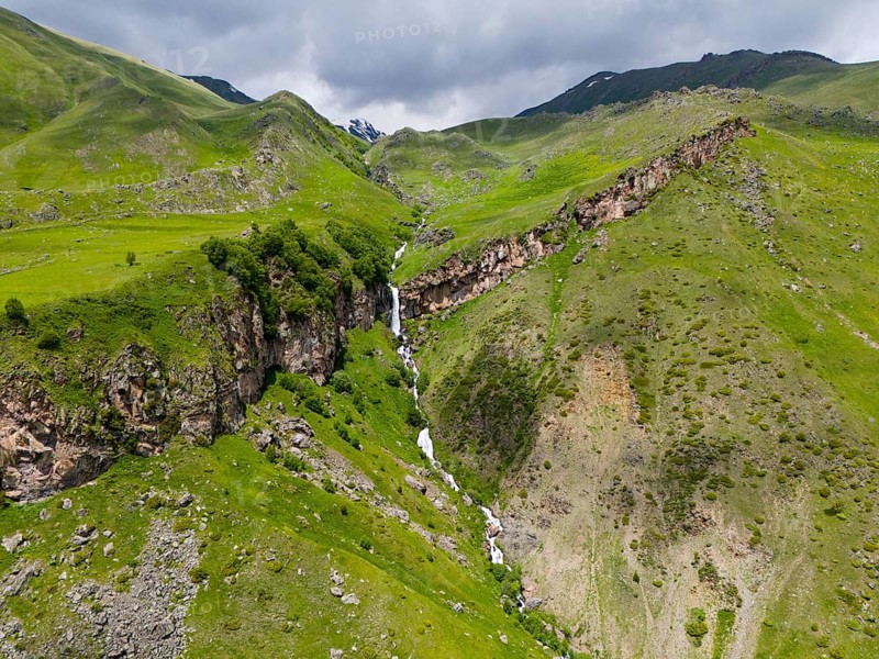Waterfall cascading down the rocky mountain face, surrounded by green landscape, aerial view, Toti Waterfall or Arsha Waterfall, Arshistskhali River, Kazbegi, Qasbegi, Stepantsminda, Georgian Military Road, Mtskheta-Mtianeti Province, High Caucasus, Georgia