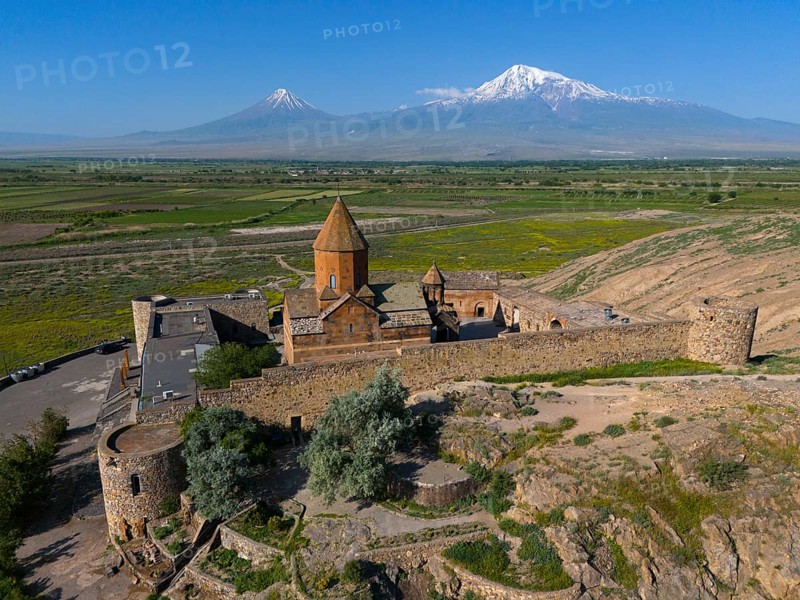 Old church in a green valley with impressive mountain ranges in the background, aerial view, Chor Wirap monastery, Chor Virap, deep dungeon, Ararat and Little Ararat in the background, located in Turkey, Ararat province, Armenia