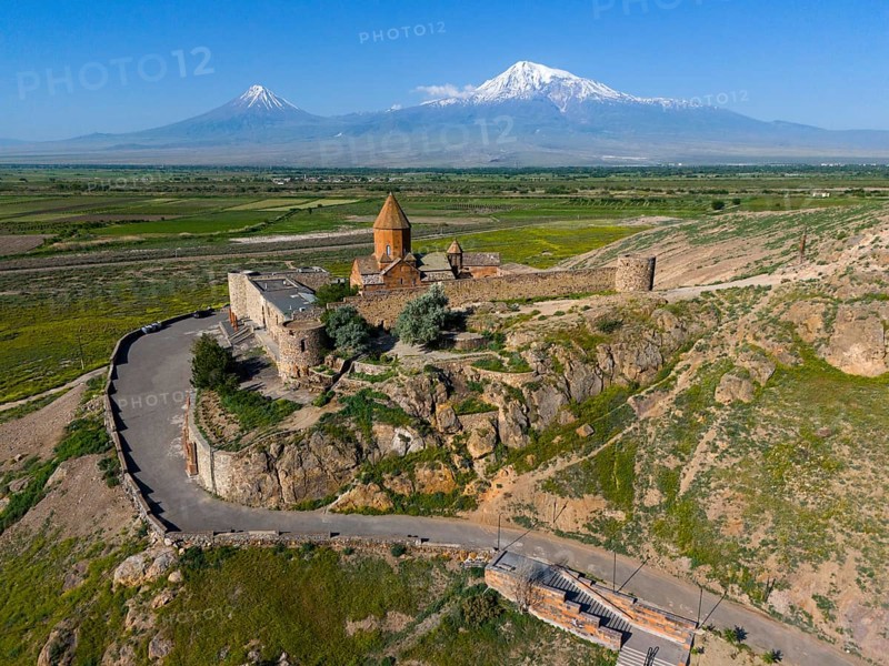 Historical church in front of majestic mountains, embedded in a green landscape with a wide sky, aerial view, monastery Chor Wirap, Chor Virap, deep dungeon, in the background the Ararat and the small Ararat, located in Turkey, Ararat province, Armenia
