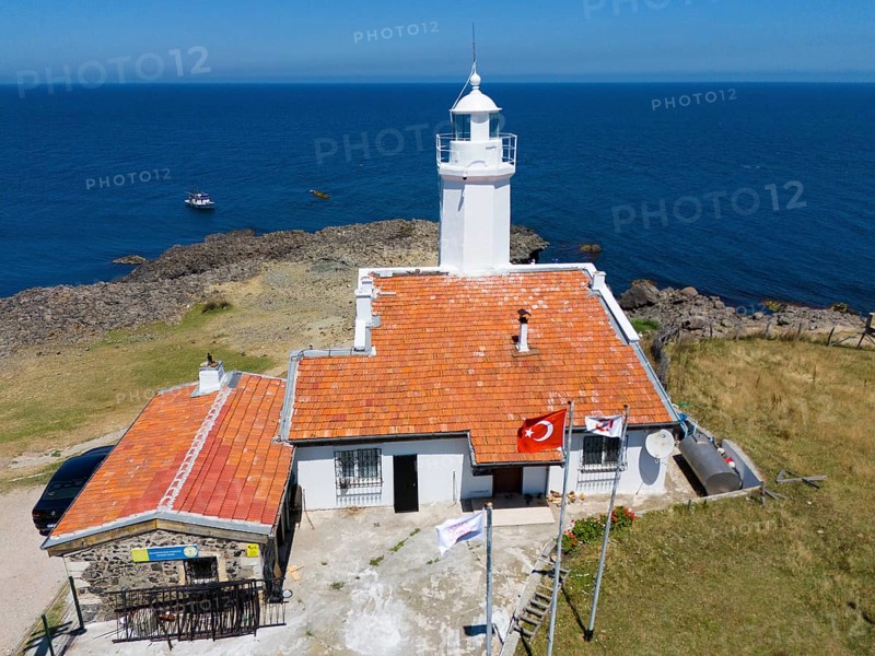 A lighthouse with terracotta roof on a rocky coast with flags and a wide ocean in the background, aerial view, lighthouse, Inceburun, Inceburun is the northernmost point of Anatolia, Sinop province, Turkey