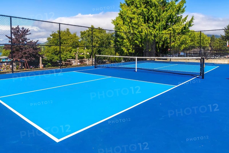 Pickleball court with net on a sunny day, showing a nearby playground in the background, offering a vibrant and inviting space for recreational activities