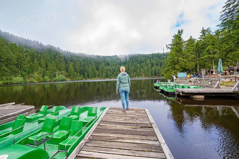 Woman on a jetty at the lake, surrounded by forest and boats under a cloudy sky, Mummelsee, Seebach, Ortenau District, Black Forest, Germany
