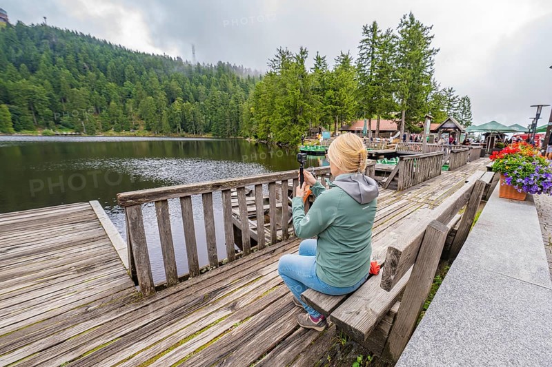Woman at the lake photographed with her smartphone from a wooden jetty, Mummelsee, Seebach, Ortenau district, Black Forest, Germany