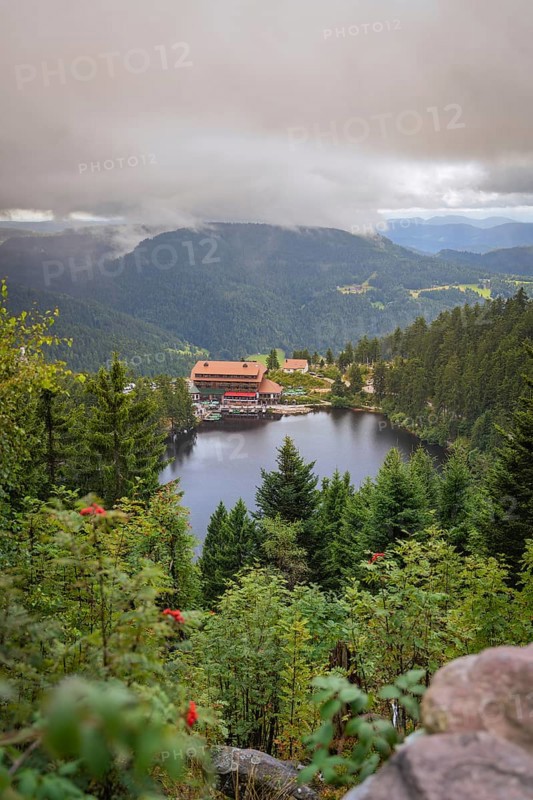 View over a lake with mountains and houses under a cloudy sky, Mummelsee, Seebach, Ortenau District, Black Forest, Germany