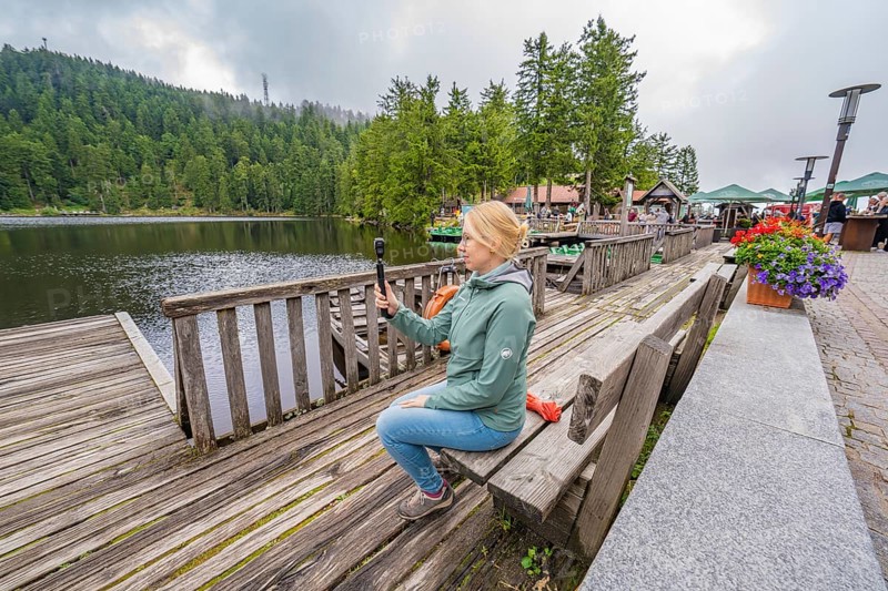 Woman on a wooden footbridge next to a lake with a camera in her hand, Mummelsee, Seebach, Ortenau District, Black Forest, Germany