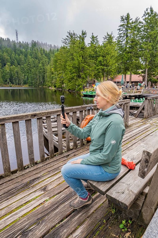 Woman sitting on a wooden footbridge and holding a camera over a lake, Mummelsee, Seebach, Ortenau district, Black Forest, Germany