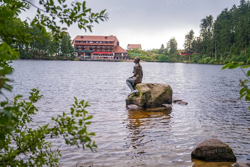 A statue sits on a rock in the lake, with a building in the background, Mummelsee, Seebach, Ortenau district, Black Forest, Germany