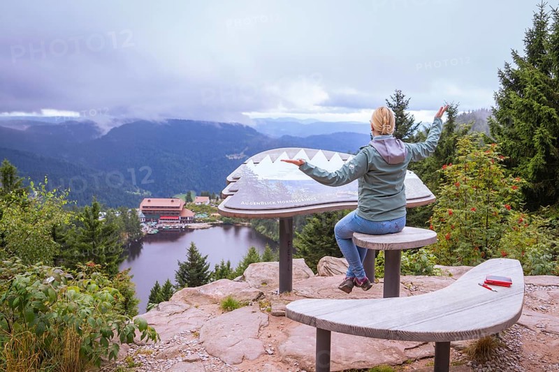 Woman sitting on a wooden bench at a viewpoint, overlooking a lake and mountains, Mummelsee, Seebach, Ortenau District, Black Forest, Germany