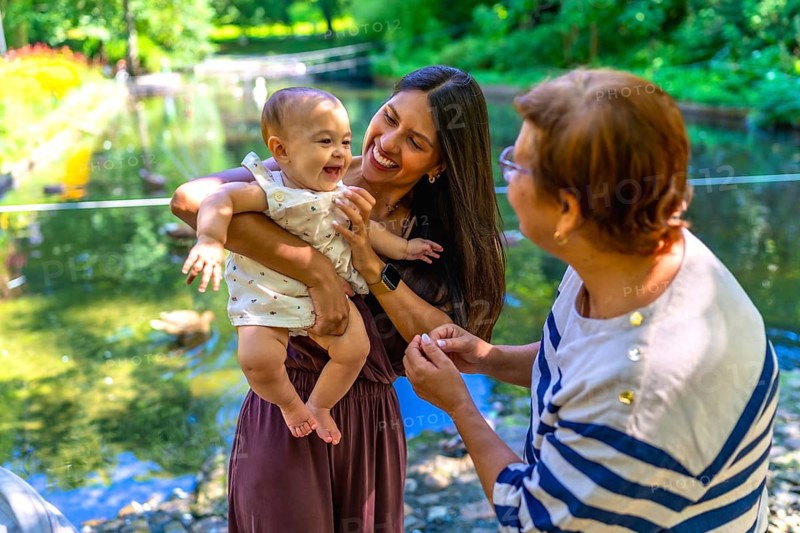 Grandmother, mother and granddaughter spending time together in a park, enjoying the summer and having fun by the pond