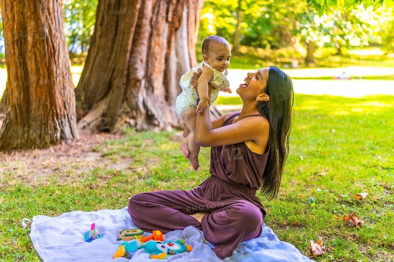 Latin mother joyfully lifting her baby daughter while sitting on a blanket in a park, enjoying playful moments and creating lasting memories