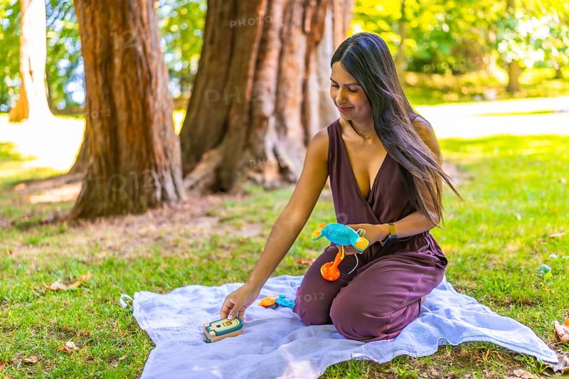 Latin mom arranging colorful baby toys on blanket in park, enjoying quality time with her child in nature