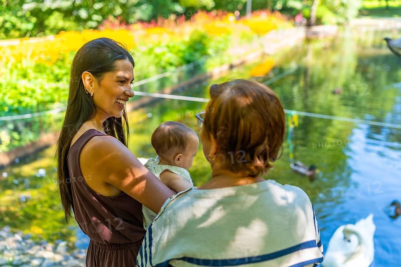 Three generations of a latin family, grandmother, mother, and baby granddaughter, spending quality time together at a park, enjoying the view of a pond with swans