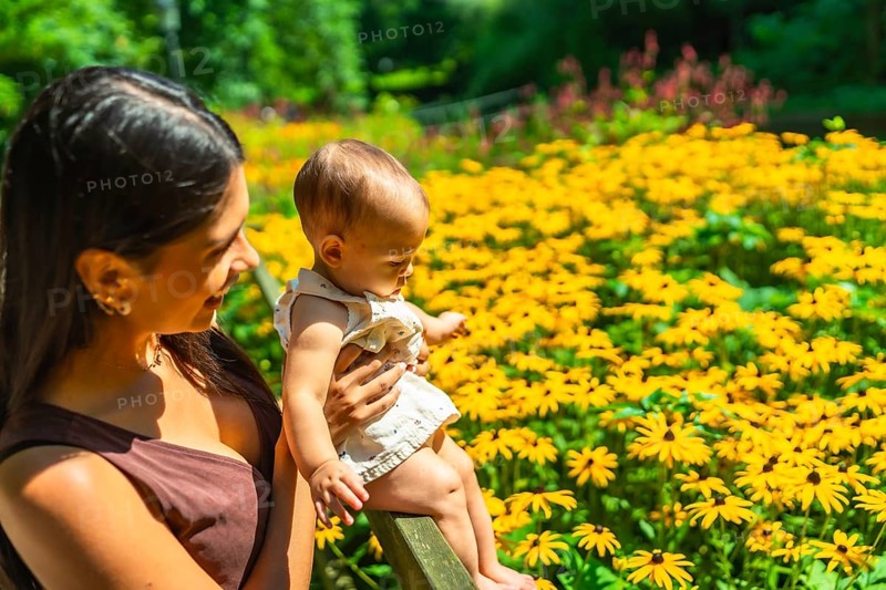Mother and baby girl enjoying a sunny day in a botanical garden, surrounded by beautiful yellow flowers