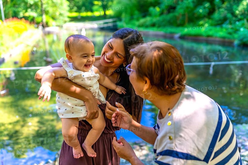 Latin family, including a grandmother, mother, and baby daughter, are enjoying quality time together in a park setting, creating cherished memories