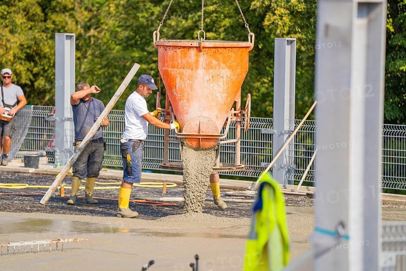 Two workers pouring concrete from large mixer tubs, surrounded by safety measures and mesh fencing, car park construction, Calw, Germany