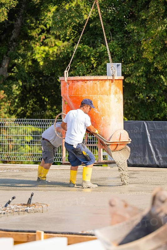 Two construction workers pouring concrete from a concrete mixer on a building site, surrounded by trees, car park construction, Calw, Germany