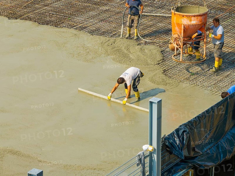 Workers smoothing concrete on a construction site while a concrete mixer stands in the background, car park construction, Calw, Germany