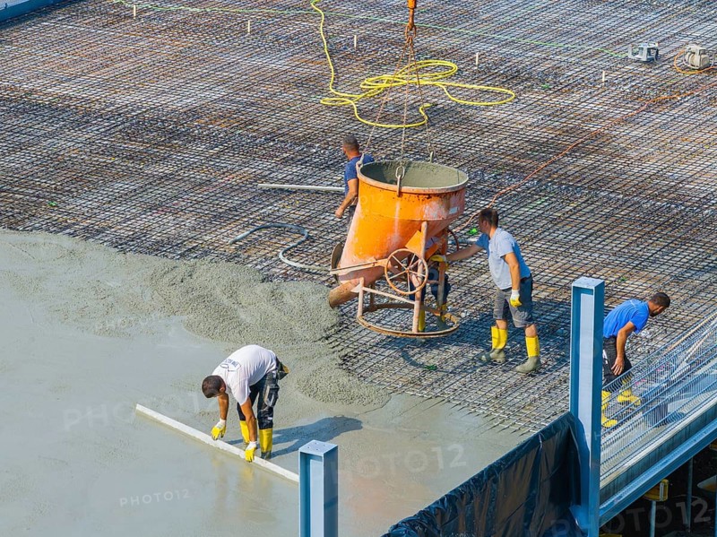 Workers pouring concrete on a construction site with concrete mixer and steel frame structure in the background, car park construction, Calw, Germany