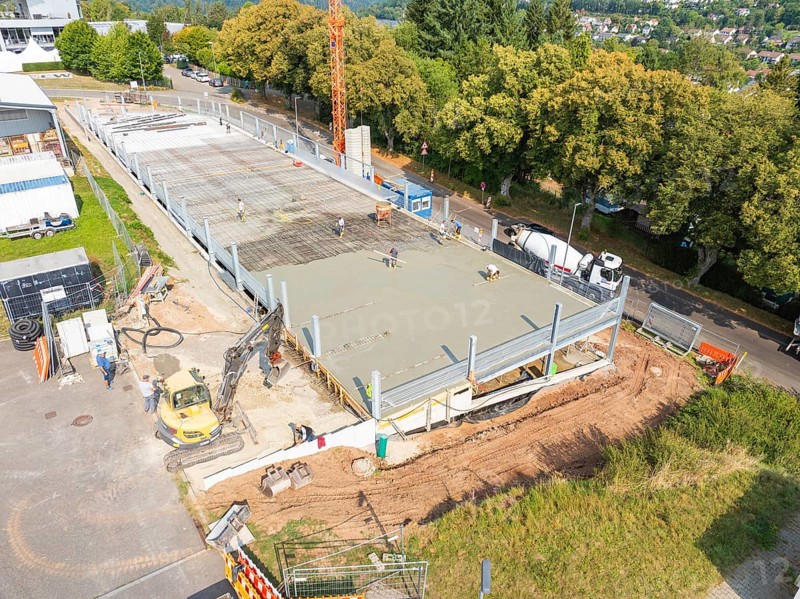 Construction site with concreted area, machines and construction workers, surrounded by green trees, car park construction, Calw, Germany